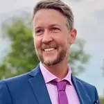 Smiling man in a blue suit and pink tie outdoors