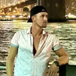 Brandon posing by the waterfront at night with a city skyline in the background