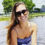 Molly smiling outdoors by the water on a sunny day
