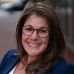 Smiling woman with glasses and brown hair wearing a navy blazer